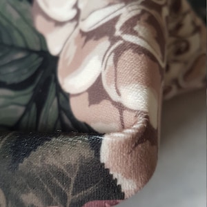 May include: Close-up of a fabric with a floral pattern. The fabric is a mix of pink, brown, and green colors. The fabric has a soft, velvety texture.