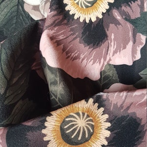 May include: Black fabric with a floral pattern featuring pink flowers with yellow centers. The fabric has a textured surface.