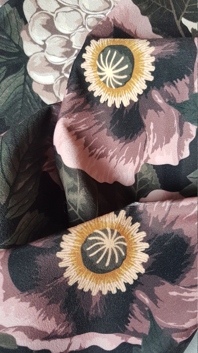 May include: Black fabric with a floral pattern featuring pink flowers with yellow centers. The fabric has a textured surface.