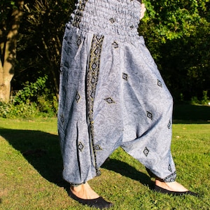 Puede incluir: Pantalones de pierna ancha de color gris y negro con un estampado floral y una cintura elástica. Los pantalones tienen un ribete negro y dorado.