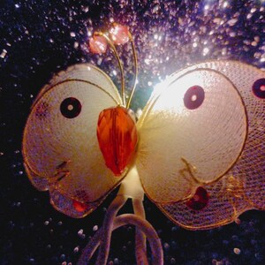 May include: A white butterfly-shaped decorative light with gold and red accents. The light is made of mesh and has a sparkly background.