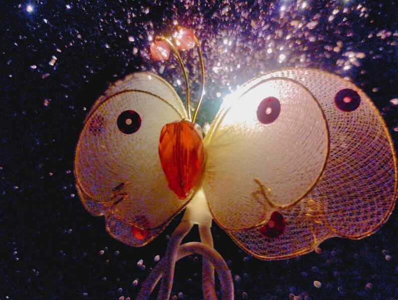 May include: A white butterfly-shaped decorative light with gold and red accents. The light is made of mesh and has a sparkly background.