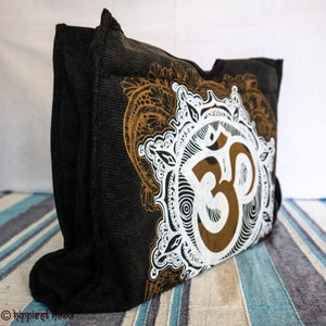 May include: Black canvas tote bag with a white and brown Om symbol surrounded by intricate floral designs.