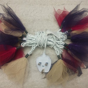 Puede incluir: Una cadena de luces con delicados tonos en forma de hoja, en tonos beige, burdeos y morado. Las luces están conectadas a un cable blanco con un enchufe del Reino Unido.