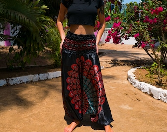 Puede incluir: Una mujer con pantalones negros con un estampado floral rojo y azul. Los pantalones son holgados y de pierna ancha. La mujer está de pie en un camino de tierra.