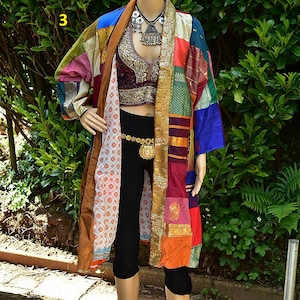 May include: A colourful patchwork kimono with a brown lining. The kimono is made of different fabrics and has a variety of colours, including red, blue, green, and yellow. The kimono is worn over a black top and black trousers.