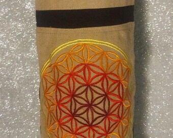May include: A black and tan yoga mat bag with a zippered pocket and an embroidered flower of life design in shades of orange, yellow, and red.