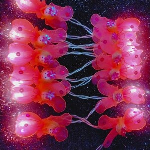 May include: A string of fairy lights with pink butterfly-shaped bulbs. The lights are strung together with clear wire and have a warm white glow.