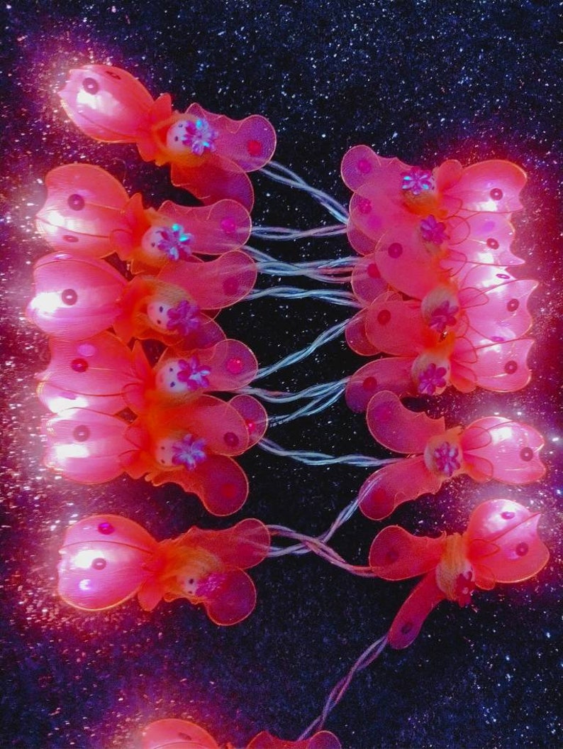 May include: A string of fairy lights with pink butterfly-shaped bulbs. The lights are strung together with clear wire and have a warm white glow.