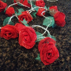 Puede incluir: Cadena de luces de hadas con bombillas rojas en forma de rosa y detalles de hojas verdes. Las luces están enhebradas con un cable transparente y son perfectas para agregar un toque de romance a cualquier espacio.