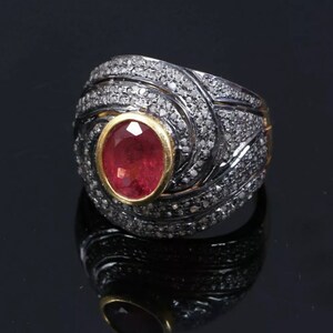 May include: A silver ring featuring a red gemstone set in a gold bezel. The ring is adorned with small diamonds.