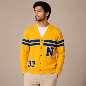 May include: A yellow cardigan with blue stripes and the letter "N" on the chest. The number "33" is on the left pocket. The cardigan has a V-neck and button closure. The person is wearing a white t-shirt underneath.