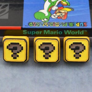 Peut inclure: Une cartouche de jeu Super Nintendo pour Super Mario World, avec trois blocs jaunes avec des points d'interrogation devant. La cartouche a une étiquette colorée avec Mario et Yoshi. La cartouche de jeu est grise.