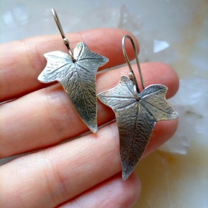 May include: Silver earrings shaped like ivy leaves with a textured surface.