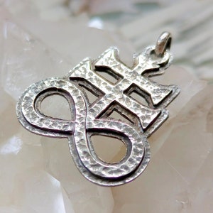 Pode incluir: Pingente de prata com um design texturizado e intrincado que apresenta uma cruz e um símbolo de infinito.