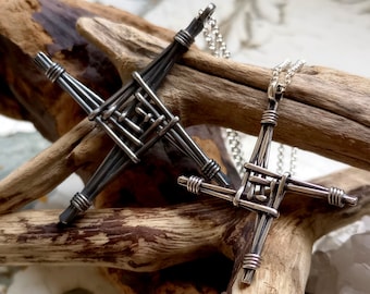 Puede incluir: Dos colgantes de nudo celta en forma de cruz de plata sobre un fondo de madera. El colgante más grande es negro y el más pequeño es plateado.