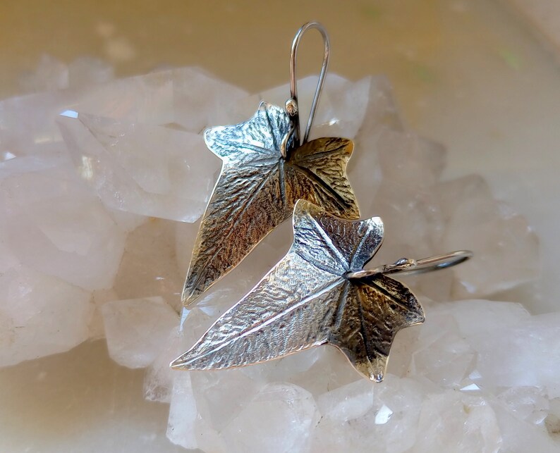 May include: A pair of silver earrings shaped like ivy leaves. The leaves are textured and have a slightly oxidized finish.