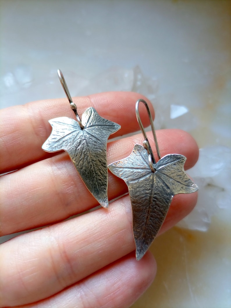 May include: Silver earrings shaped like ivy leaves with a textured surface.