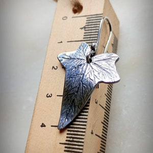 May include: Silver ivy leaf earrings with a textured surface. The earrings are approximately 3 cm long and are shown next to a ruler.