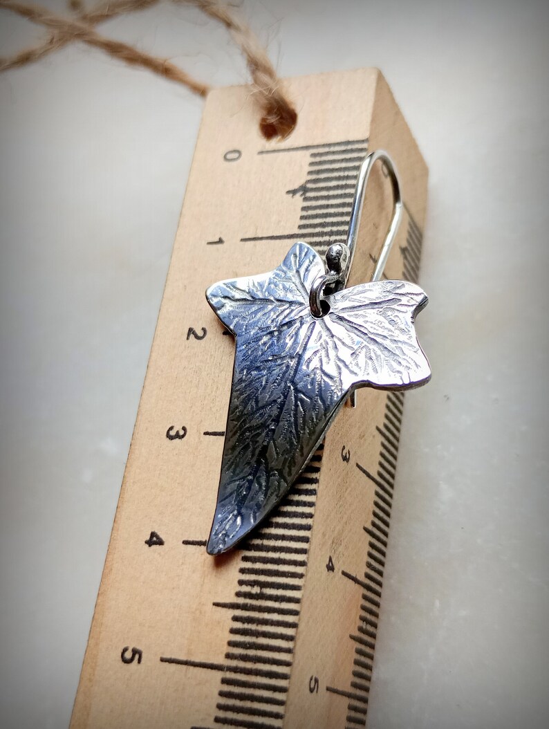 May include: Silver ivy leaf earrings with a textured surface. The earrings are approximately 3 cm long and are shown next to a ruler.
