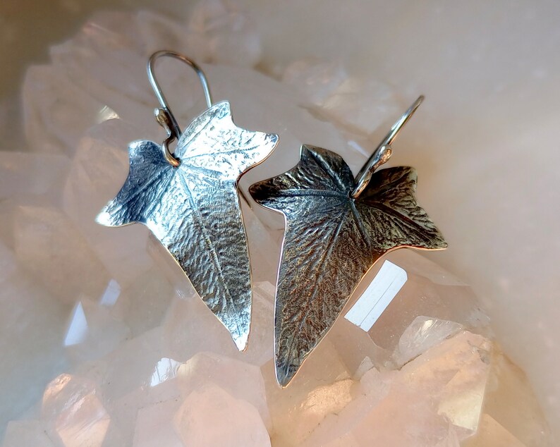 May include: A pair of silver earrings shaped like ivy leaves. The leaves have a textured surface and are detailed with veins.