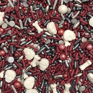 May include: A mix of red, silver, and white sprinkles, including skull and bone shapes, for decorating cakes and cupcakes.