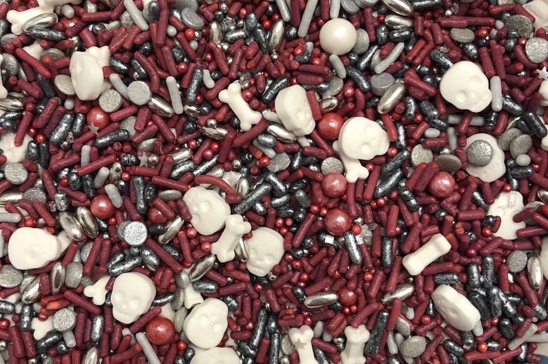May include: A mix of red, silver, and white sprinkles, including skull and bone shapes, for decorating cakes and cupcakes.