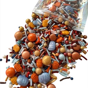 May include: A clear plastic bag filled with colorful sprinkles, including blue, orange, brown, gold, and white. The sprinkles are in the shape of pumpkins, balls, and long, thin sticks. The bag is labeled "Sprinkle Obsession".