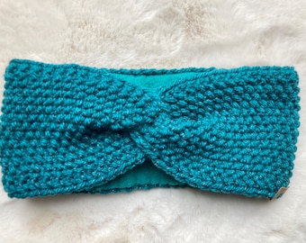 Op de afbeelding: Tealgekleurde gebreide hoofdband met een gedraaid knoopontwerp. De hoofdband is gemaakt van een getextureerd gebreid materiaal en heeft een zachte, tealgekleurde voering. Dit accessoire is ontworpen om de oren warm te houden.