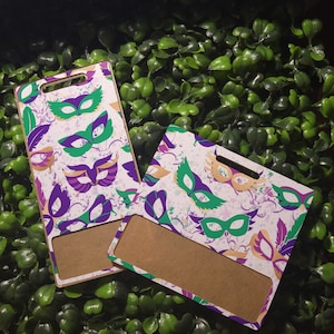May include: Two blank, rectangular, wooden name tags with a white background and a colorful pattern of purple, green, and gold masquerade masks. The name tags have a clear plastic window for inserting text.