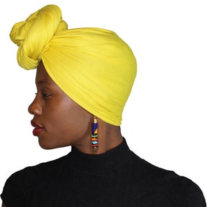 May include: A woman wearing a bright yellow turban with a long beaded earring. The earring is made of colorful beads and has a gold top.