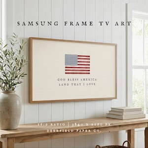 May include: Samsung Frame TV art featuring an American flag design. The artwork displays a red and blue flag with the text "GOD BLESS AMERICA LAND THAT I LOVE". The frame has a 16:9 ratio and 3840 x 2160 px resolution.