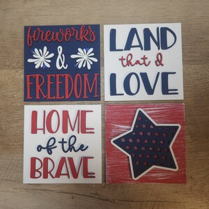 May include: Four wooden signs with red, white, and blue paint and text. The signs read "fireworks & freedom", "land that I love", "home of the brave", and a star with a red, white, and blue pattern.