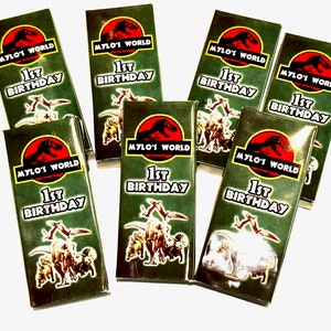 K&ouml;nnte beinhalten: Ein Set mit sieben gr&uuml;nen und roten Geschenkboxen mit Dinosaurier-Motiv. Die Boxen haben eine Grafik eines Dinosauriers und den Text "Mylo's World 1st Birthday".