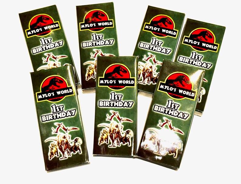 K&ouml;nnte beinhalten: Ein Set mit sieben gr&uuml;nen und roten Geschenkboxen mit Dinosaurier-Motiv. Die Boxen haben eine Grafik eines Dinosauriers und den Text "Mylo's World 1st Birthday".