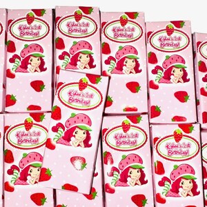 K&ouml;nnte beinhalten: Ein Stapel rosa und wei&szlig;er Geschenkboxen mit einem Erdbeer-Shortcake-Charakterdesign. Die Boxen haben ein wei&szlig;es Oval mit dem Text "Kilee's 1st Birthday!" in gr&uuml;ner und roter Schrift.
