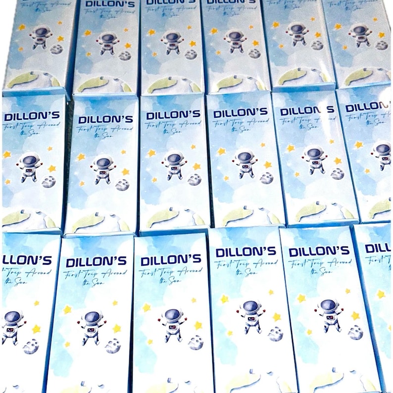 K&ouml;nnte beinhalten: Eine Sammlung von 12 blauen und wei&szlig;en Geschenkboxen mit einem Astronauten-Design. Die Boxen tragen den Text "Dillon's First Trip Around the Sun".
