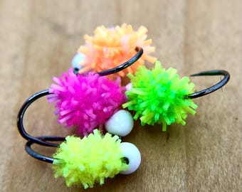 May include: Four colourful fly fishing lures with white beads. The lures are made of fluffy material in shades of pink, green, yellow, and orange.