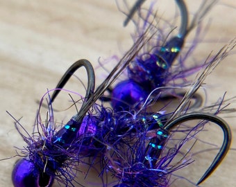 May include: Three purple and iridescent fly fishing lures with black hooks and a black and white logo that reads "Jacob's Fork Fly Tying U.S."