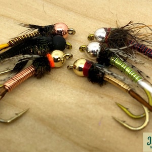 May include: Assortment of six fly fishing lures with different coloured beads and metallic bodies. The lures have black, brown, and white feathers.