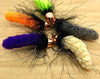 May include: Five fly fishing lures with black feathers and different coloured fuzzy bodies. The bodies are green, orange, purple, grey, and cream.
