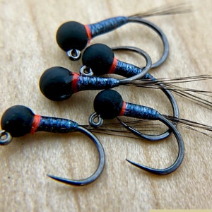 May include: Close-up of five black and blue fly fishing lures with red accents. The lures have black beads and are tied on hooks. The lures are on a wooden surface.