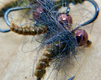 May include: Close-up of a fly fishing lure with brown and gold accents, a dark blue body, and a brown and gold segmented body. The lure is tied on a hook with a black shank.