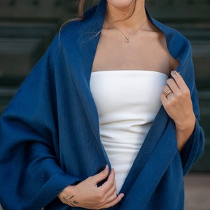 May include: A woman wearing a white strapless top and a dark blue shawl. She is wearing a gold necklace and rings on her fingers.