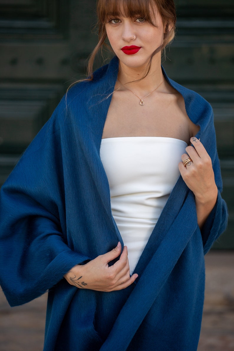 May include: A woman wearing a white strapless top and a dark blue shawl. She is wearing a gold necklace and rings on her fingers.