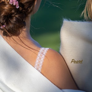 May include: Two women wearing white shawls, one ivory and one pearl. The woman in the ivory shawl has a floral hair clip and a lace strap on her shoulder.