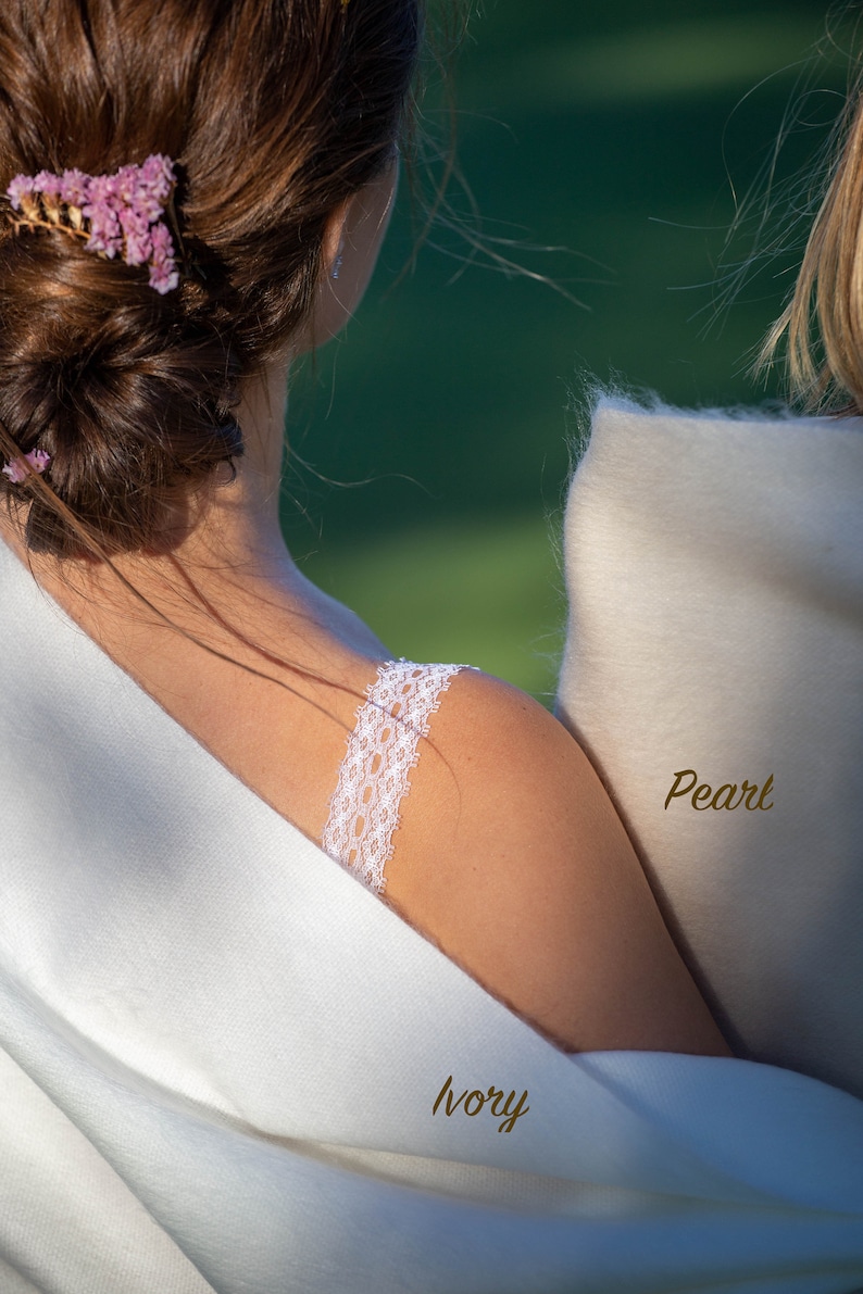 May include: Two women wearing white shawls, one ivory and one pearl. The woman in the ivory shawl has a floral hair clip and a lace strap on her shoulder.