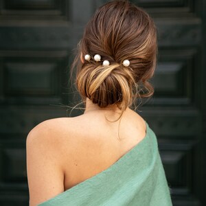 Pu&ograve; includere: Una donna con i capelli castani raccolti in uno chignon con fermagli per capelli di perle. Indossa una stola verde chiaro.