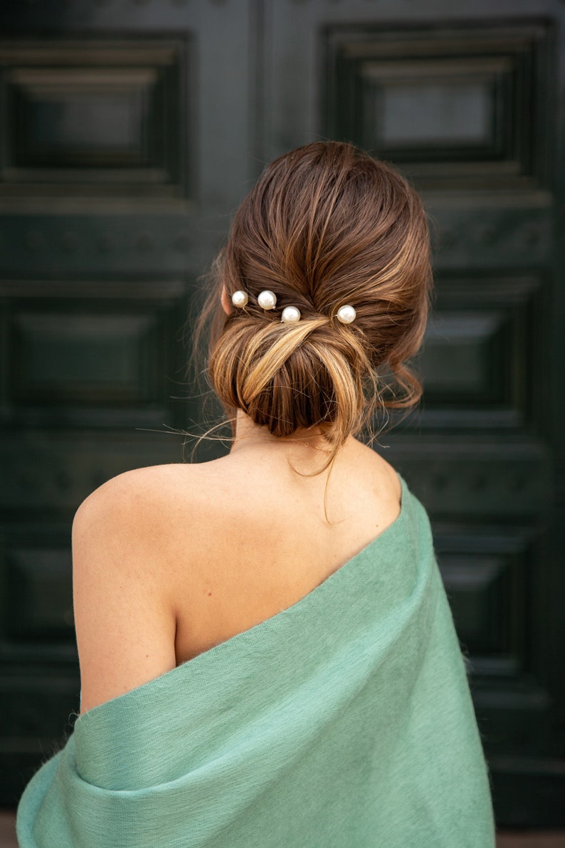 Pu&ograve; includere: Una donna con i capelli castani raccolti in uno chignon con fermagli per capelli di perle. Indossa una stola verde chiaro.