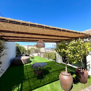 May include: A patio with a brown pergola, a small table and chairs, a hot tub, and two potted lemon trees. The patio is covered in artificial grass.